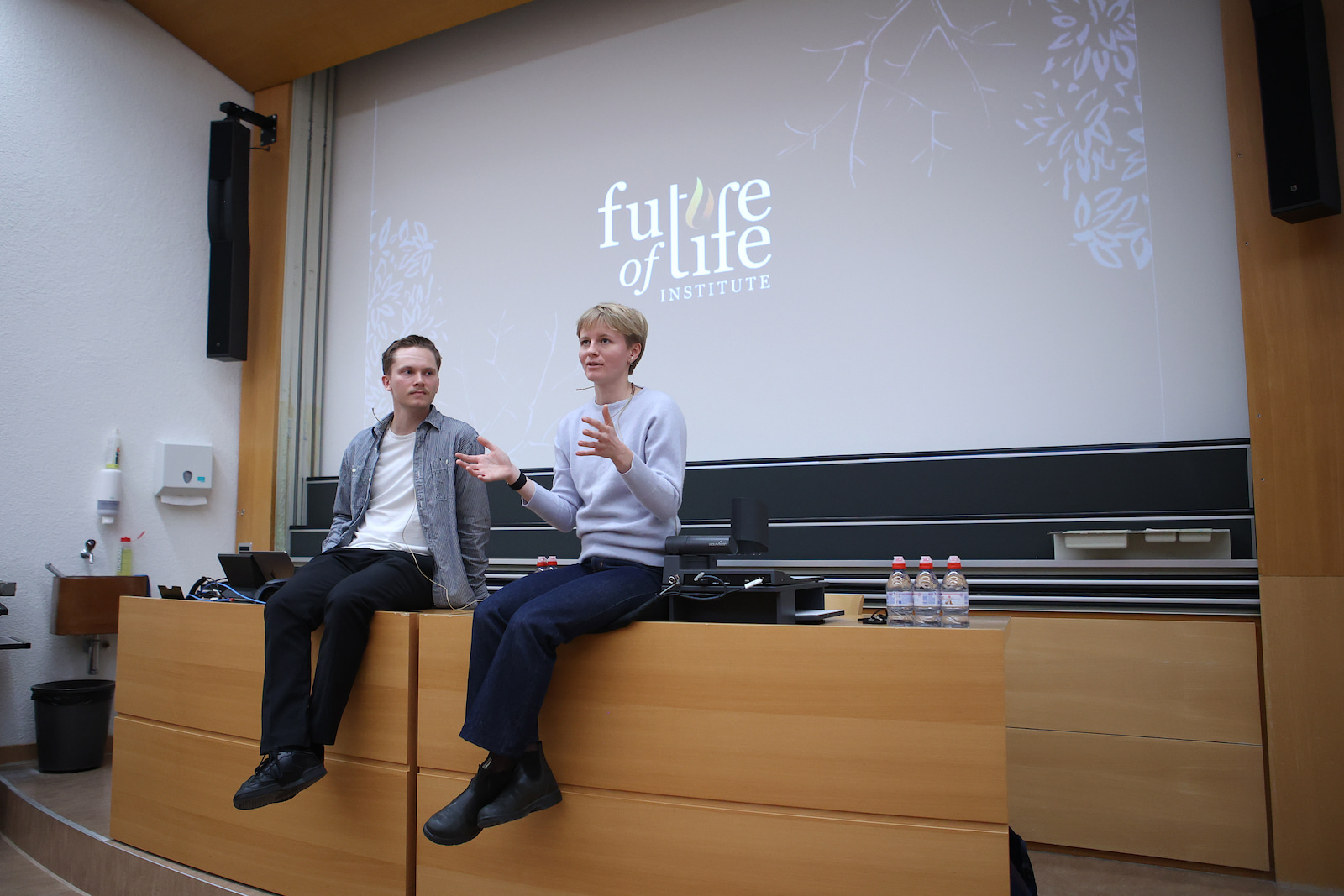 Two speakers seated on the stage edge during a Future of Life Institute session